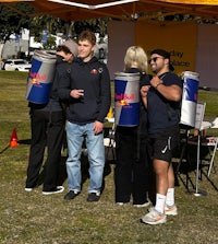 a group of people standing under a tent with red bull cans