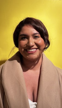 a woman in a tan coat smiling in front of a yellow background